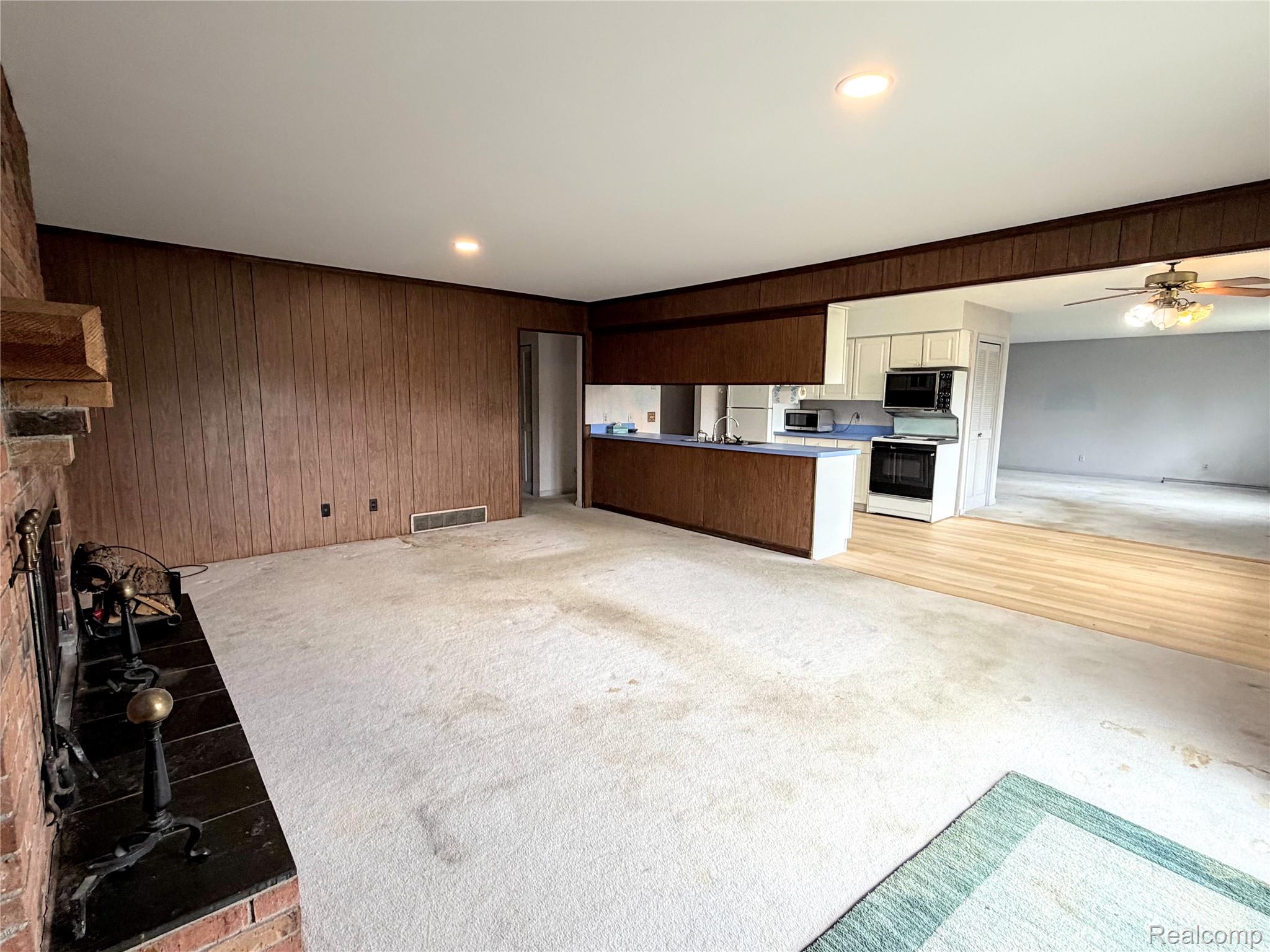 8079 Farley Road Pinckney, MI 48169 - Photo 40 of 43 Kitchen with open floor plan, light colored carpet, ceiling fan, white range oven, and wood walls