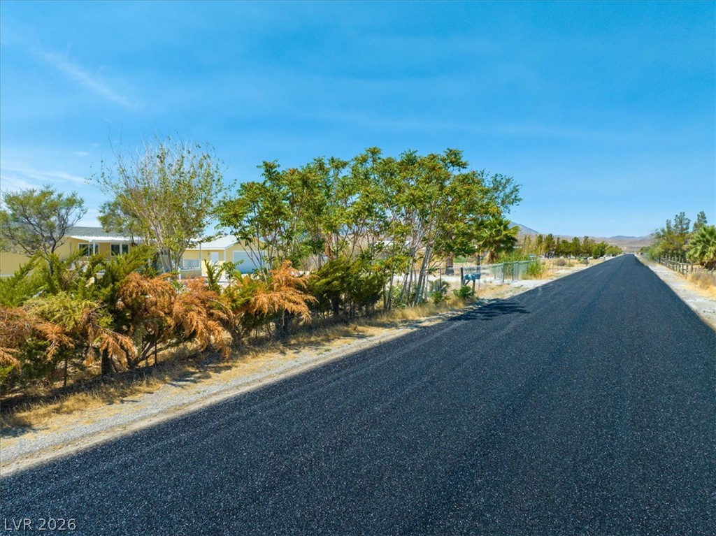 4081 Retread Road Pahrump, NV 89048 - Photo 75 of 98 A newly paved road extends into the distance, framed by natural desert flora and a distant residential structure.