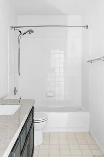 a bathroom with a granite countertop bathtub shower sink vanity and toilet