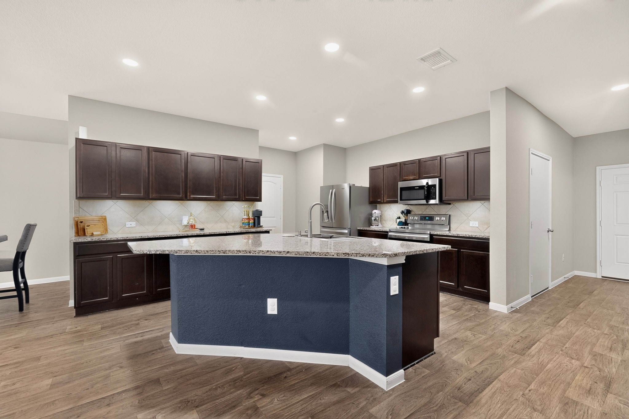 11612 Andesite Road Manor, TX 78653 - Photo 16 of 40 Rich wood cabinetry and a central island highlight this functional open kitchen design.