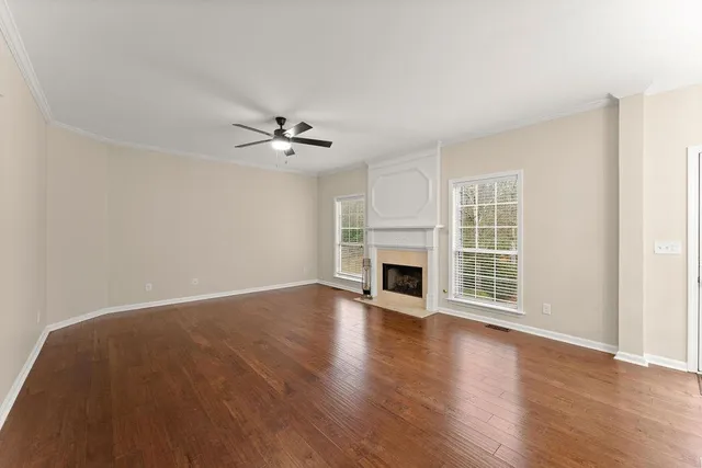 an empty room with wooden floor fireplace and windows