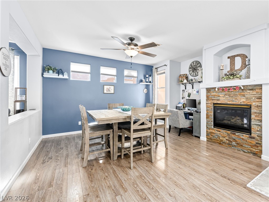 Dining space with baseboards, wood Living area with baseboards, a stone fireplace, and luxury vinyl plank flooring