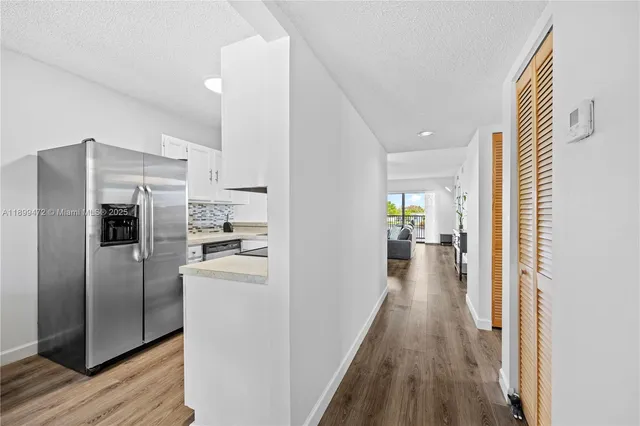 a view of a kitchen with a refrigerator a stove top oven hallway and wooden floor