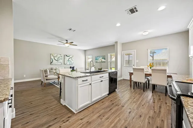 a kitchen with stainless steel appliances granite countertop a stove top oven a sink dishwasher a dining table and chairs with wooden floor