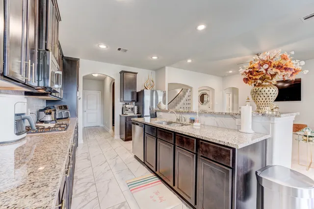 a kitchen with stainless steel appliances kitchen island granite countertop a refrigerator a sink dishwasher and a stove with wooden floor