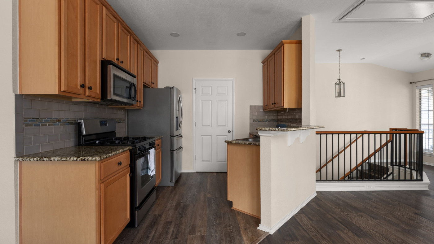 14815 Avery Ranch Boulevard, Unit 1401 Austin, TX 78717 - Photo 11 of 38 Kitchen featuring wood-finish flooring, granite-style countertops, stainless steel appliances, a tiled backsplash, and light wood cabinetry
