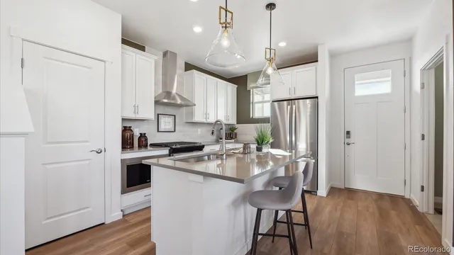 a kitchen with stainless steel appliances granite countertop a refrigerator a sink dishwasher a stove and white cabinets with wooden floor