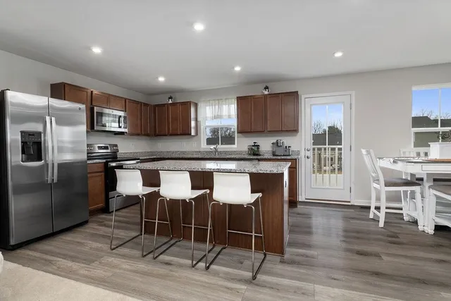 a kitchen with stainless steel appliances granite countertop a stove a refrigerator a sink and a dining table with wooden floor