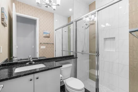 a bathroom with a granite countertop sink a toilet a mirror a vanity and shower