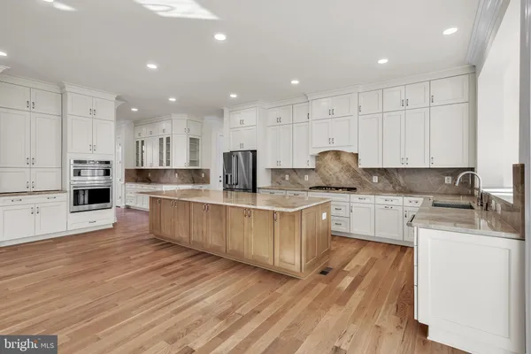 a large kitchen with stainless steel appliances granite countertop a stove a sink a refrigerator and white cabinets with wooden floor