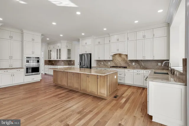 a large kitchen with stainless steel appliances granite countertop a stove a sink a refrigerator and white cabinets with wooden floor