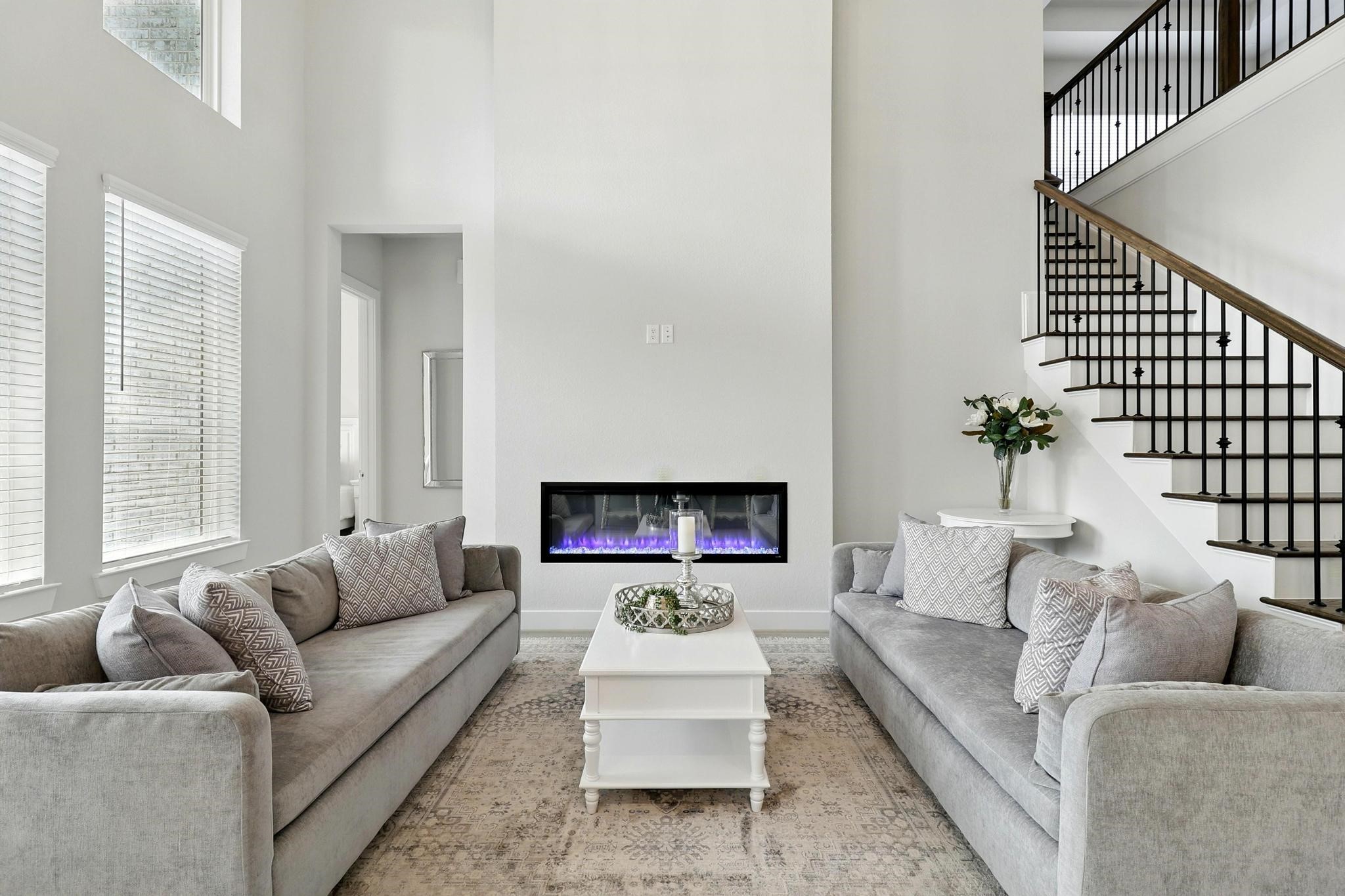26923 Arethusa Court Spring, TX 77389 - Photo 5 of 44 This inviting living room features high ceilings, large windows, and a modern electric fireplace. and an open staircase with a sleek railing, creating a bright and spacious atmosphere.