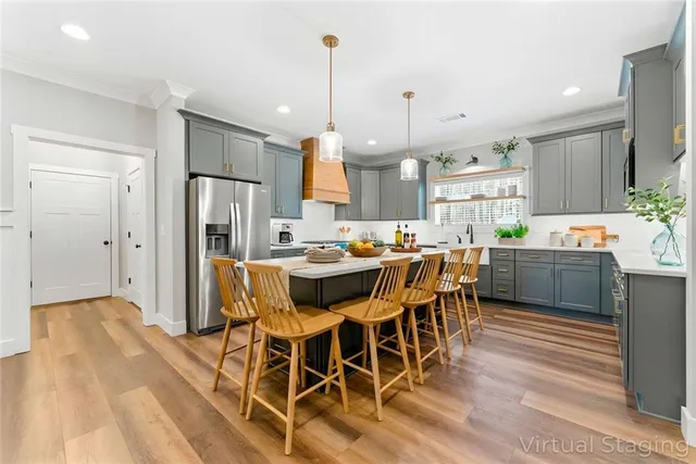 a kitchen with stainless steel appliances a refrigerator a sink dishwasher a dining table and chairs with wooden floor