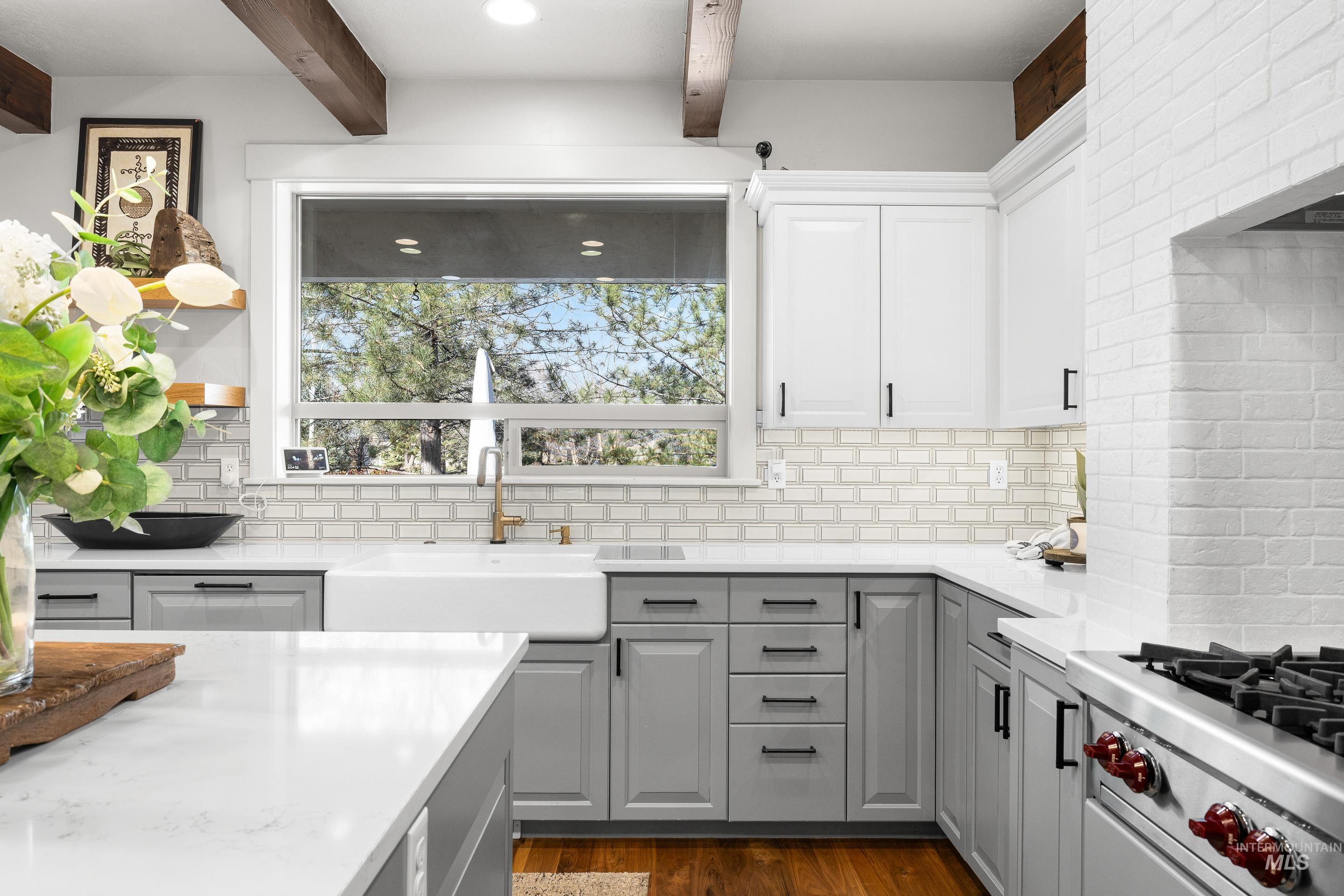 1166 East Rivers End Drive Eagle, ID 83616 - Photo 13 of 50 Two tone kitchen with light stone countertops, stainless steel gas cooktop, dark wood-style flooring, beamed ceiling, and backsplash