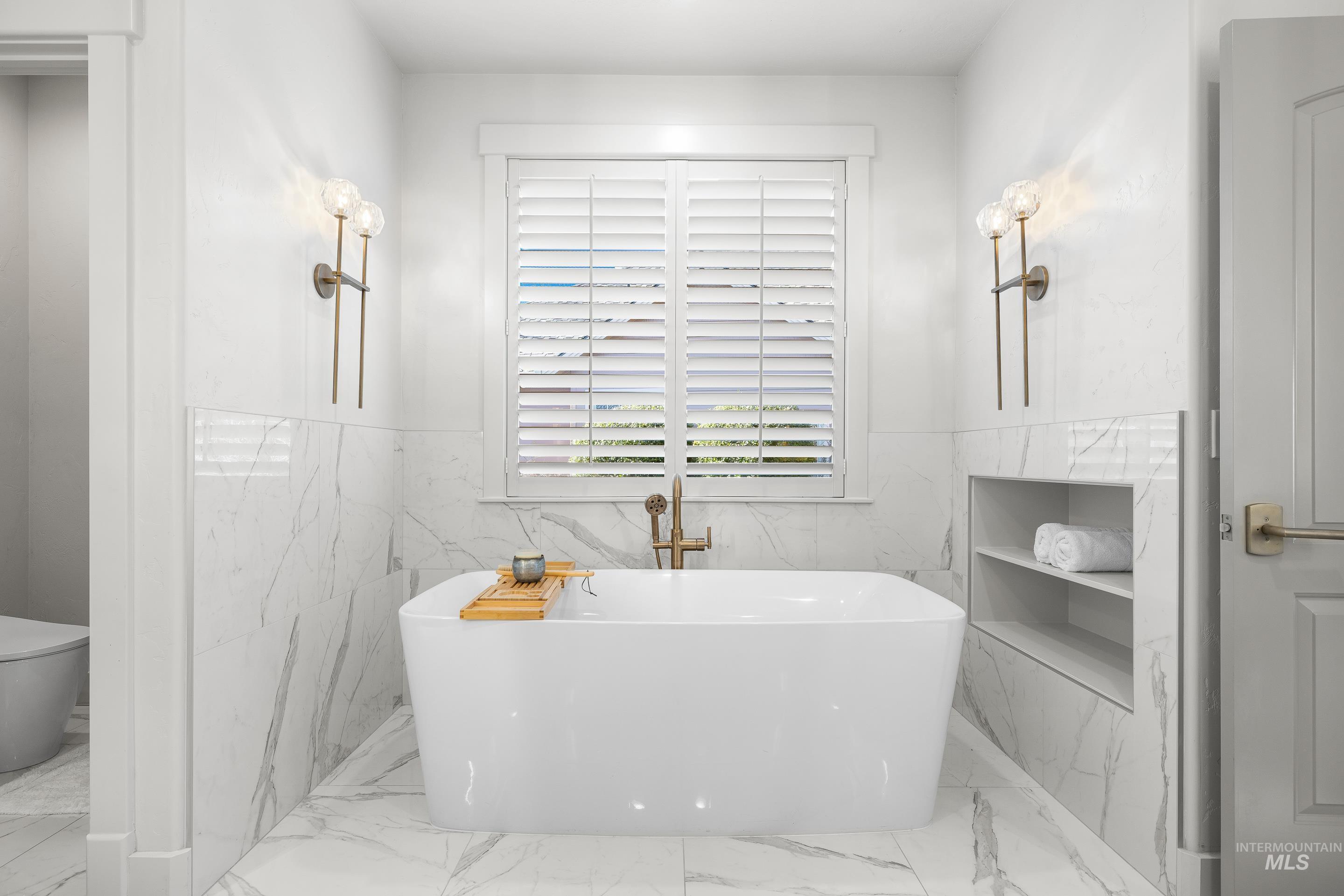 1166 East Rivers End Drive Eagle, ID 83616 - Photo 28 of 50 Full bath featuring light marble finish floors, a soaking tub, tile walls, and a wainscoted wall