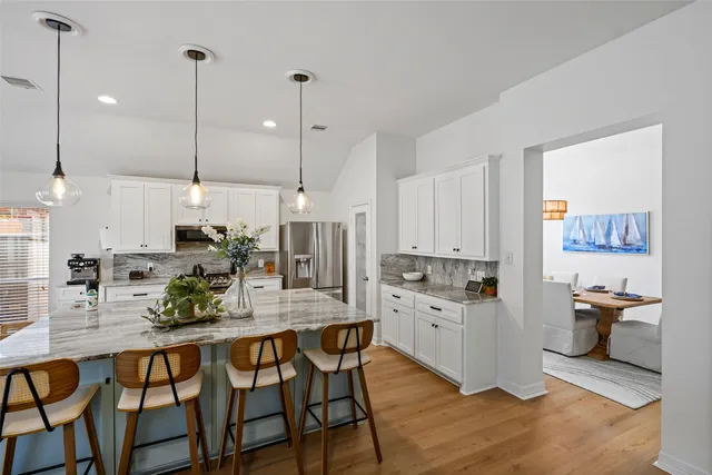 a kitchen with stainless steel appliances kitchen island granite countertop a stove a sink and white cabinets with wooden floor