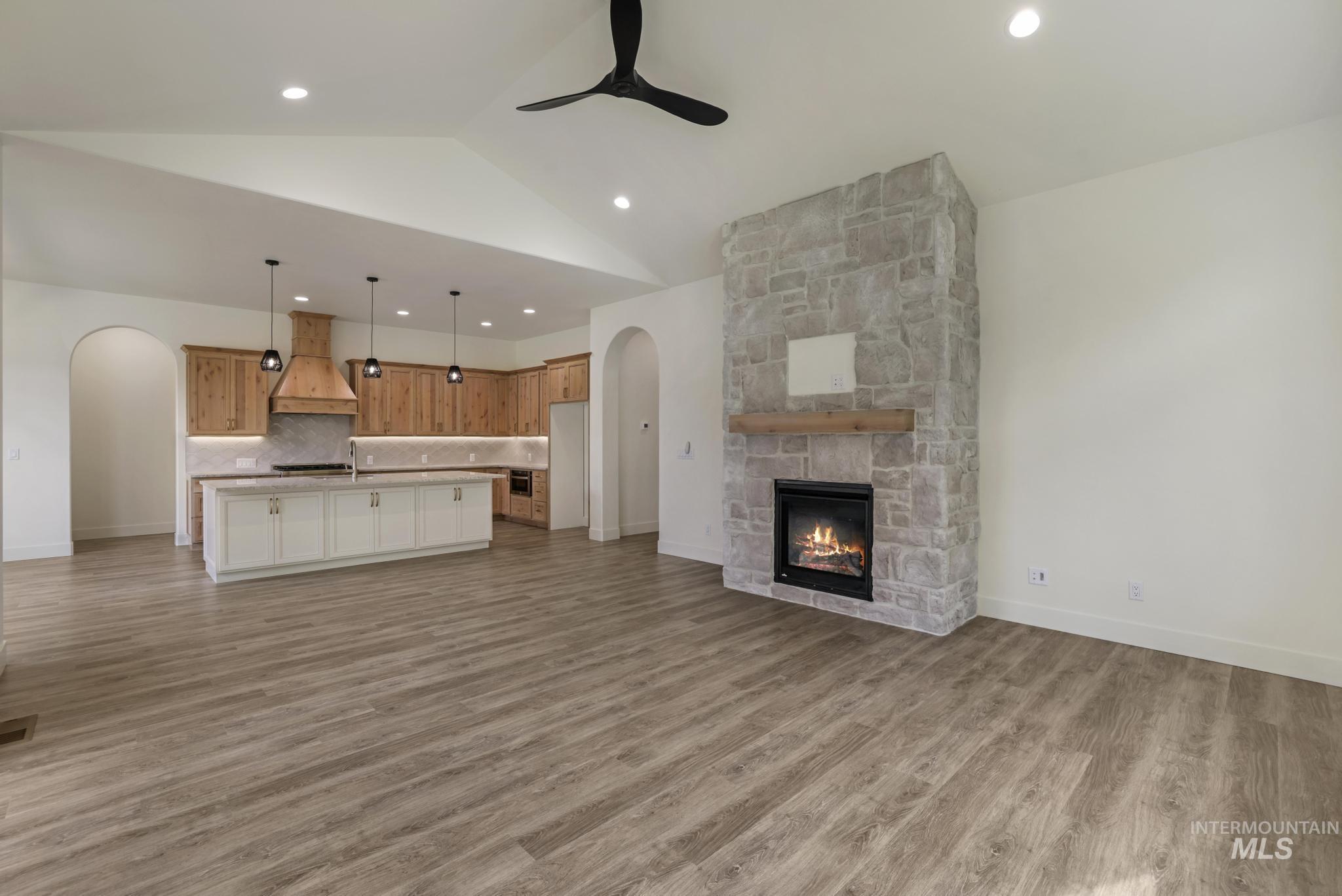 542 Falling Leaf Lane Twin Falls, ID 83301 - Photo 13 of 38 Unfurnished living room featuring arched walkways, light wood finished floors, a fireplace, lofted ceiling, and a ceiling fan