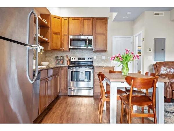 a kitchen with stainless steel appliances granite countertop a refrigerator a stove top oven a dining table and chairs with wooden floor