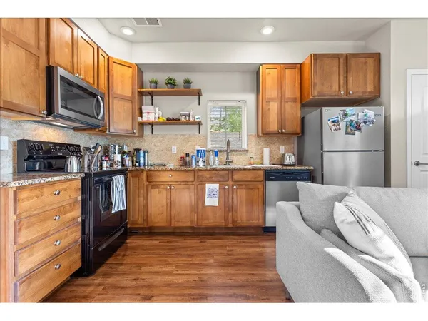 a kitchen with stainless steel appliances granite countertop a refrigerator a stove top oven a sink and dishwasher with wooden floor