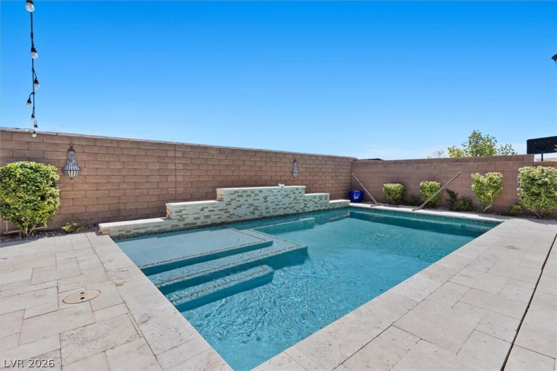 The pool's raised stacked stone water feature wall and clear turquoise water anchor the private backyard.