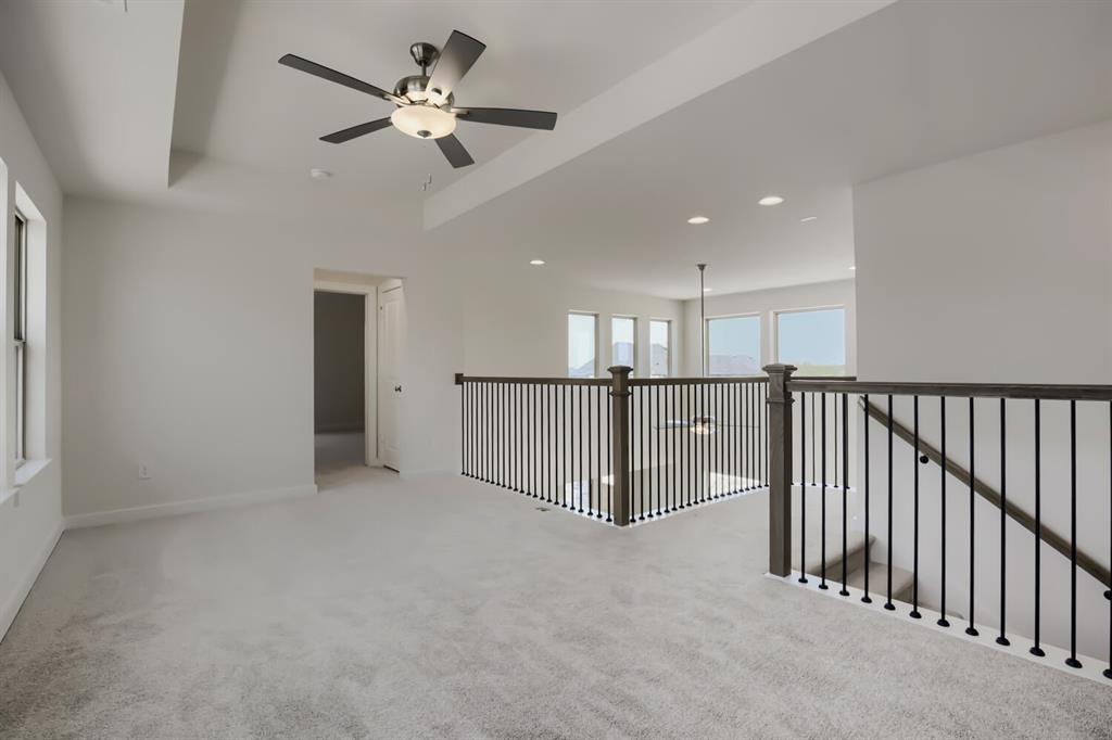 828 Stone Grv Road Lavon, TX 75166 - Photo 8 of 27 Carpeted loft area featuring a tray ceiling with a modern ceiling fan, large windows, and a dark wood and iron spindle railing overlooking an open space with additional windows