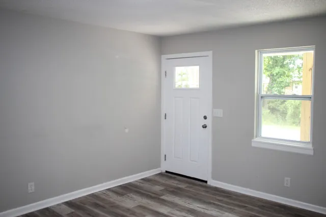 a view of an empty room with wooden floor and a window