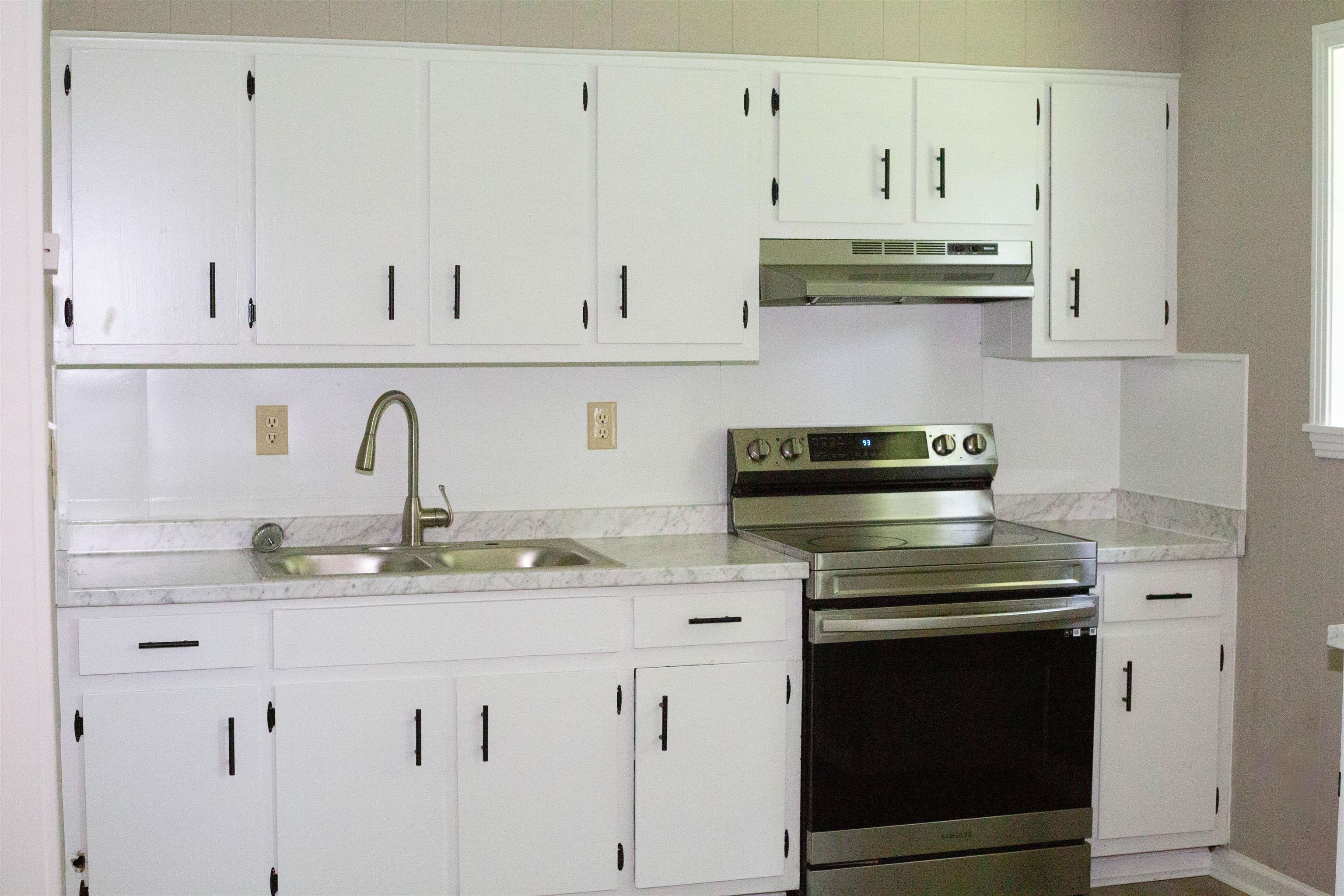 583 Armstrong Road Drummonds, TN 38023 - Photo 5 of 14 Kitchen featuring white cabinetry with black hardware, stainless steel sink with gooseneck faucet, light-toned countertops, and a modern stainless steel range with overhead ventilation