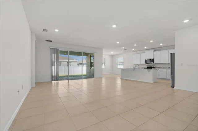 a view of an empty room with kitchen and window