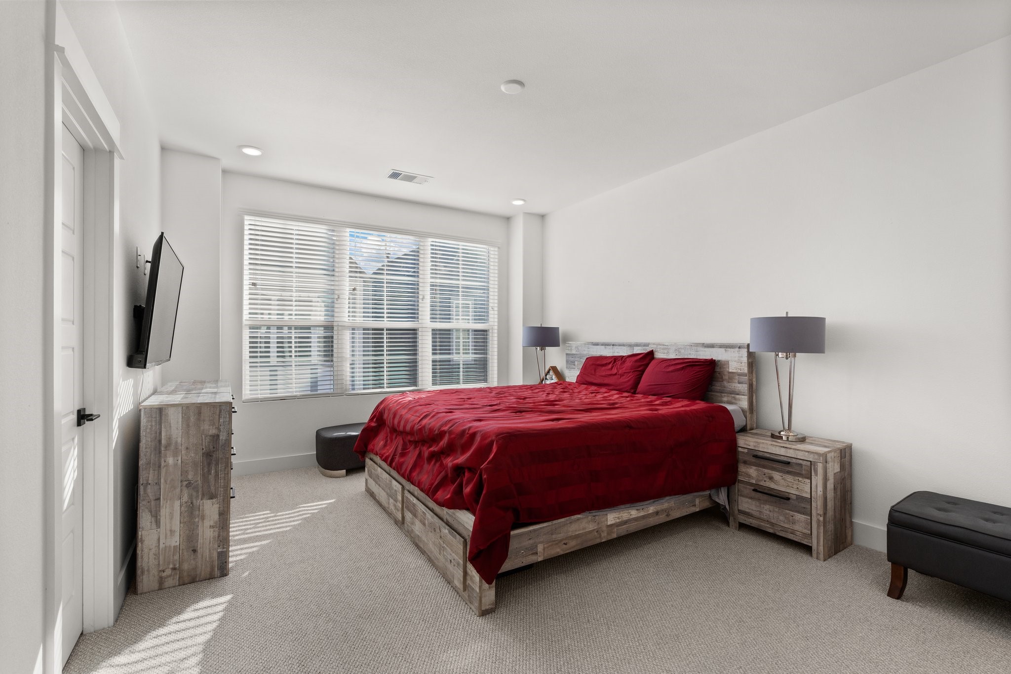 2928 Stevens Street Houston, TX 77026 - Photo 12 of 30 Bright and spacious bedroom with large windows, neutral walls, and carpeted flooring. Features a rustic wood bed set with red bedding, matching nightstands, and a mounted TV for convenience.