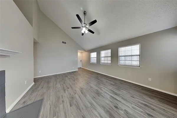 an empty room with wooden floor fan and windows