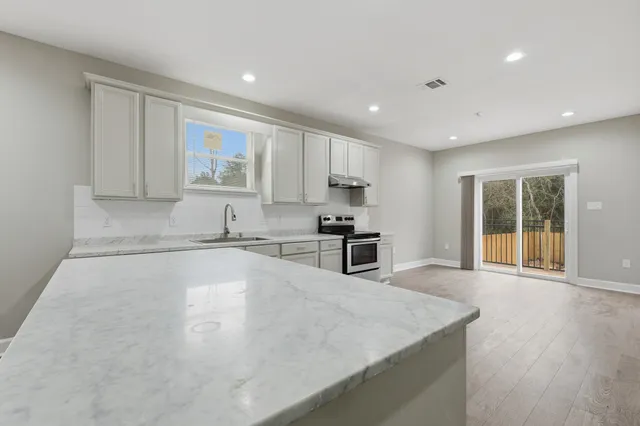 a large kitchen with stainless steel appliances granite countertop a stove a sink a refrigerator and white cabinets with wooden floor