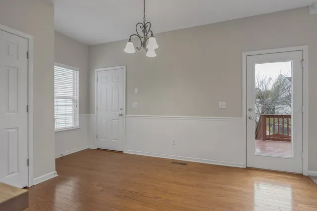 an empty room with wooden floor chandelier and windows