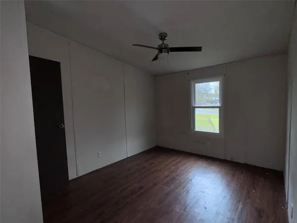 an empty room with wooden floor fan and windows