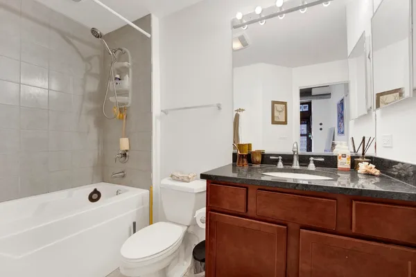 a bathroom with a granite countertop sink a toilet a mirror a bathtub and shower