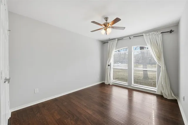 an empty room with wooden floor fan and windows