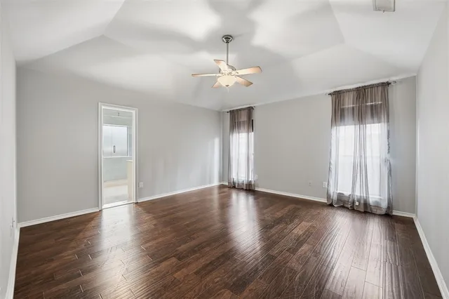 an empty room with wooden floor ceiling fan and windows
