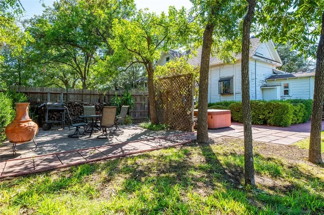 a view of a backyard with table and chairs potted plants and large tree