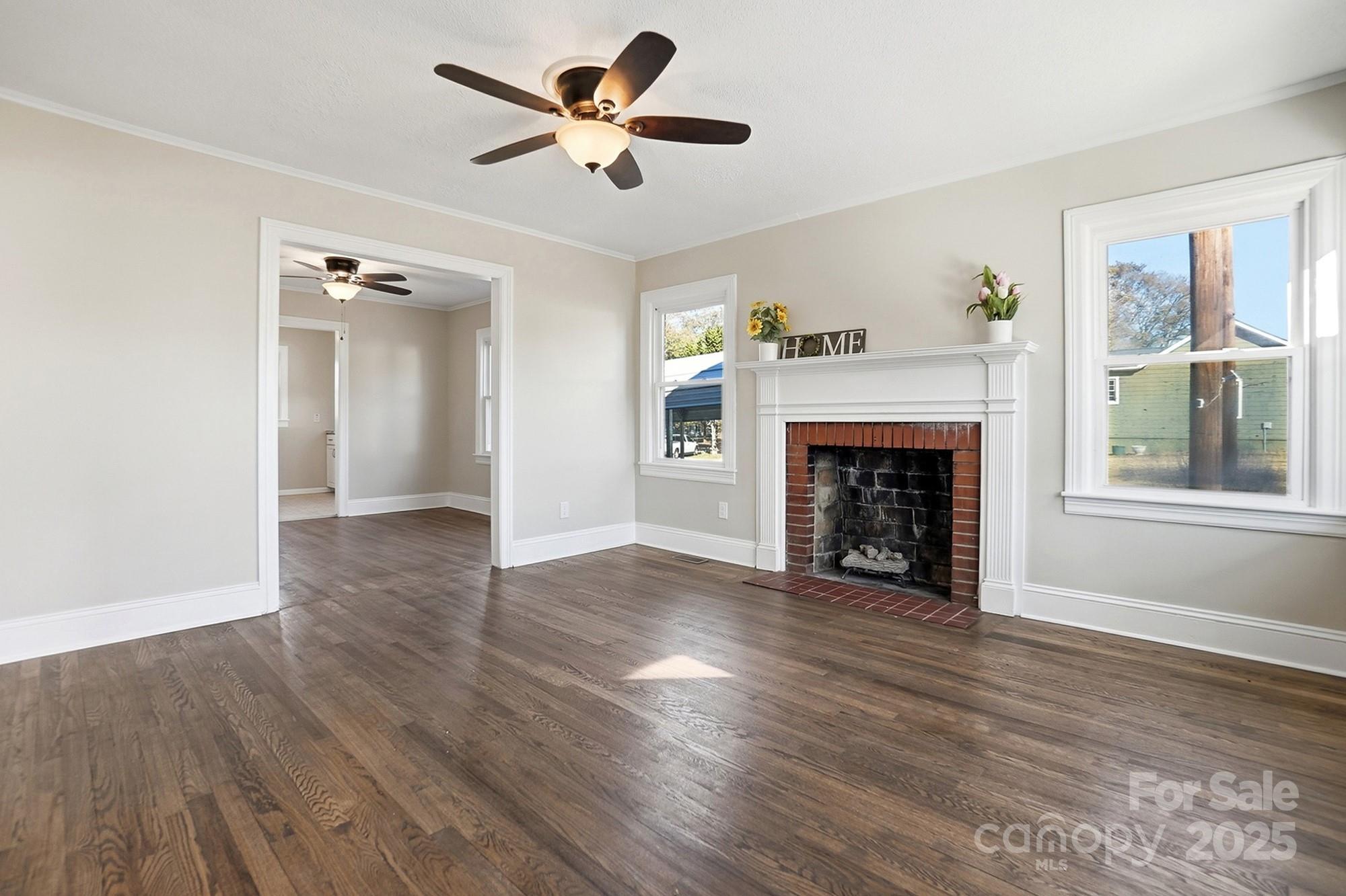 412 Ridge Street Stanley, NC 28164 - Photo 5 of 30 an empty room with windows a fireplace a ceiling fan and wooden floor