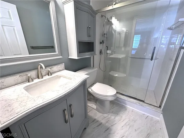 a bathroom with a granite countertop sink a toilet a mirror and shower