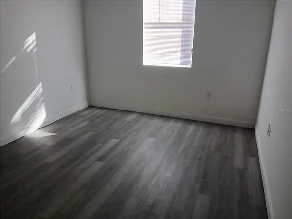 a view of an empty room with wooden floor and a window