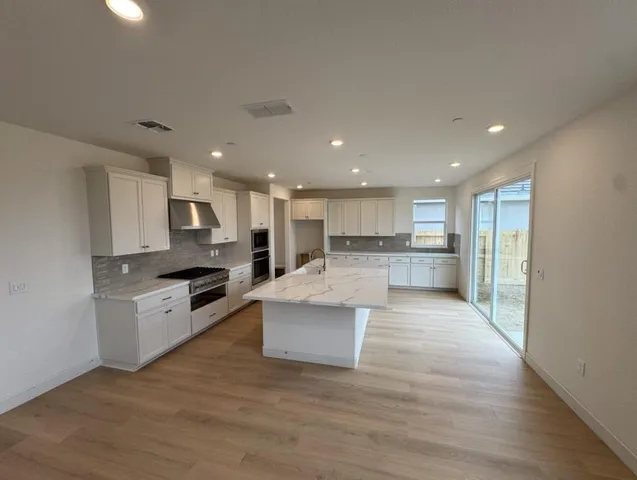 a large white kitchen with kitchen island a stove a sink a refrigerator and white cabinets with wooden floor