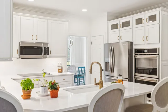 a kitchen with stainless steel appliances kitchen island granite countertop a refrigerator a stove a sink a oven with white cabinets and wooden floor