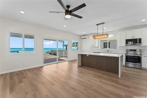 a large kitchen with stainless steel appliances kitchen island granite countertop a stove a sink a refrigerator and white cabinets with wooden floor