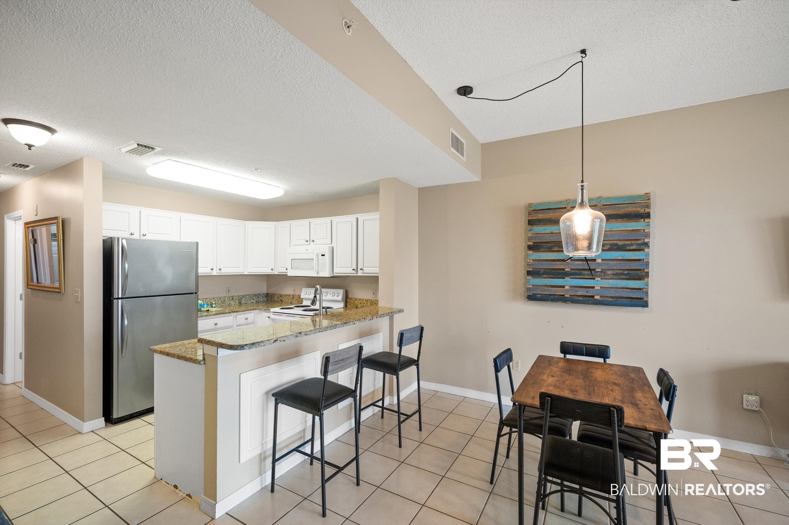 1380 Fort Morgan Road, Unit 106 Gulf Shores, AL 36542 - Photo 4 of 20 Kitchen featuring visible vents, a kitchen bar, light stone counters, white appliances, and white cabinetry