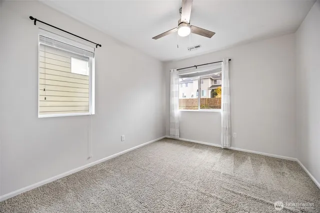 an empty room with chandelier fan and windows