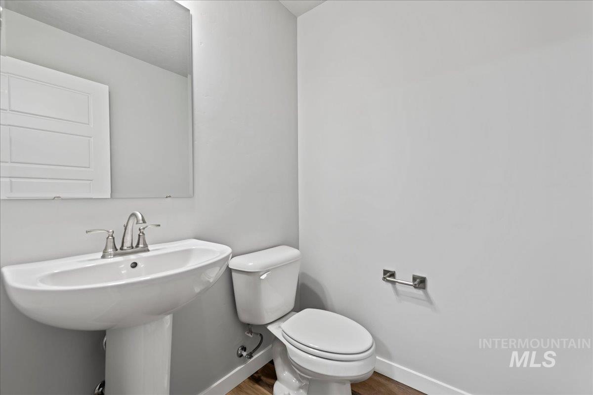 12535 West Victory Road Boise, ID 83709 - Photo 22 of 25 Pedestal sink with chrome faucet, toilet, wall-mounted mirror, and wood-finish flooring