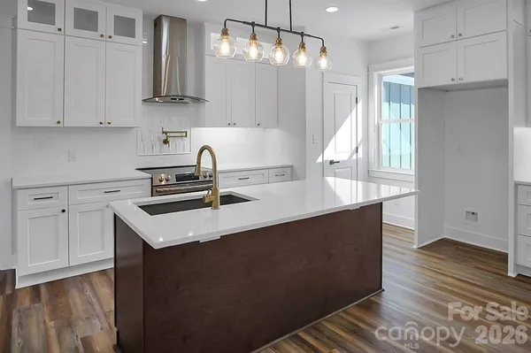a kitchen with stainless steel appliances granite countertop a sink stove and white cabinets with wooden floor