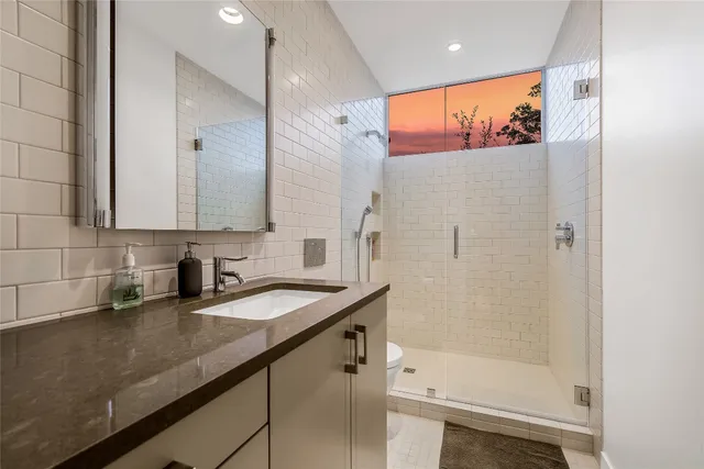 a bathroom with a granite countertop sink a toilet a mirror and shower