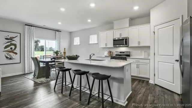 a kitchen with stainless steel appliances granite countertop a stove a sink a microwave a refrigerator and white cabinets with wooden floor