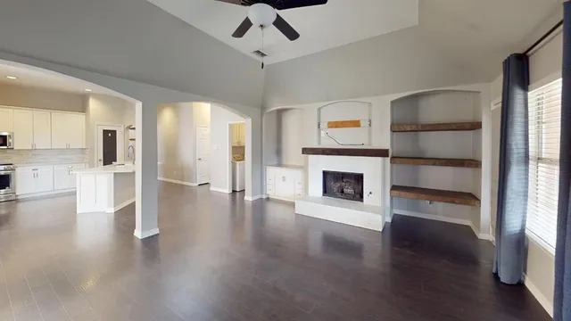 a view of a livingroom with a fireplace a ceiling fan a kitchen refrigerator and a window